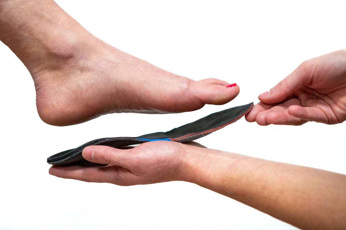 Pedorthist fitting a custom orthotic insole beneath a patient's bare foot to assess support and positioning